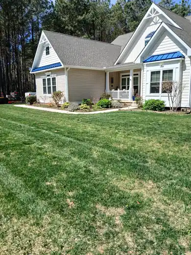 A freshly mowed lawn in front of a cream house with blue roof trim