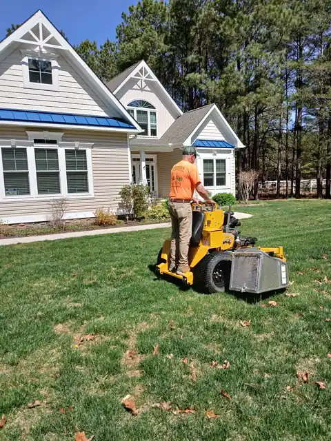 A Hertzog crew member on a yellow stand-on mower crossing a front lawn