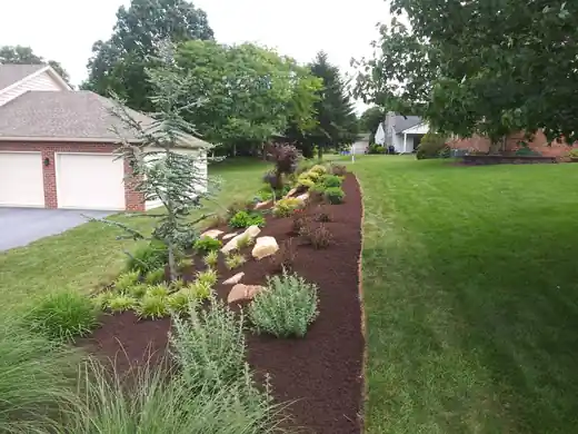 Finished planted bed along a lawn with boulders and grasses