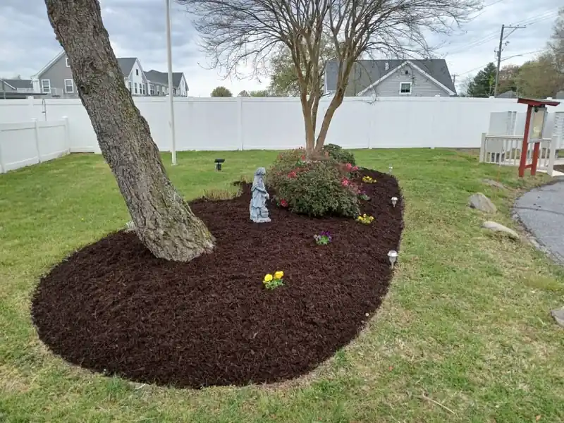 A cleared yard with a fresh mulch ring around a tree beside a white vinyl fence
